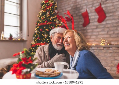 Senior couple sitting by nicely decorated Christmas tree, having fun while celebrating Christmas at home, singing Christmas songs - Powered by Shutterstock