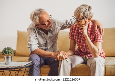 Senior couple sitting in living room. Woman is sad and worried and man is consoling her. - Powered by Shutterstock