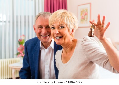 Senior Couple Sitting On The Bed In The Hotel Room And The Woman Has A Key In Her Hand