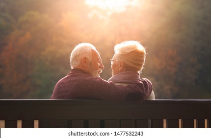 Senior couple sitting on bench in autumn park and looking sunset - Powered by Shutterstock