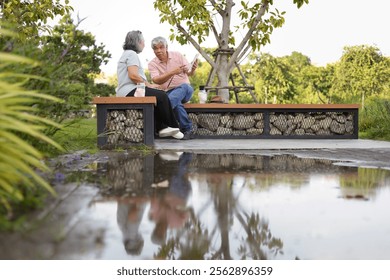 Senior couple sitting on a bench in park, Asian senior man and woman use laptop and digital tablet in park - Powered by Shutterstock