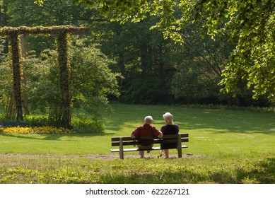 Senior Couple Sitting On Bench In A Park Photographed From Behind