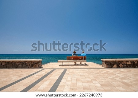 A senior couple sitting on a bench on the beach in the midday sun