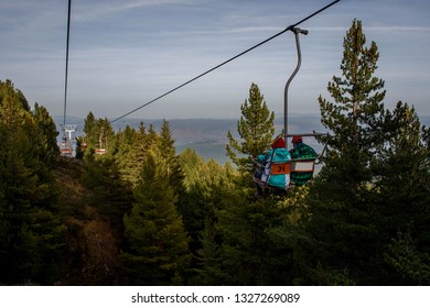 Senior Couple Is Sitting On A Chair Lift In The Forest Mountains On A Sunny Day In Pirin National Park, Bulgaria