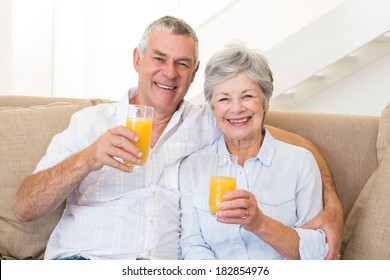 Senior Couple Sitting On Couch Drinking Orange Juice At Home In Living Room