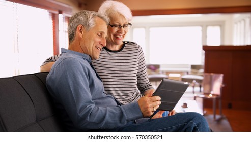 Senior Couple Sitting On Couch Watching Videos On Tablet