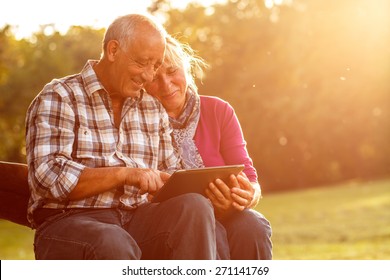 Senior couple sitting on a park bench on sunny autumn day with tablet and relaxing.
 - Shutterstock ID 271141769
