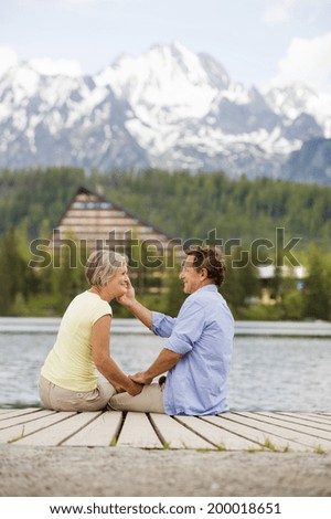 Senior couple sitting on pier above the mountain lake with mountains in background