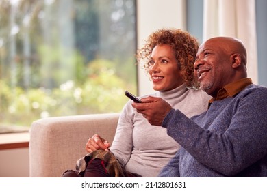 Senior Couple Sitting On Sofa At Home Watching TV Together