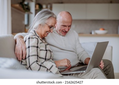 Senior couple sitting on sofa and using laptop together. - Powered by Shutterstock