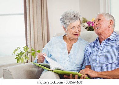 Senior couple sitting on sofa and reading a book in living room - Powered by Shutterstock