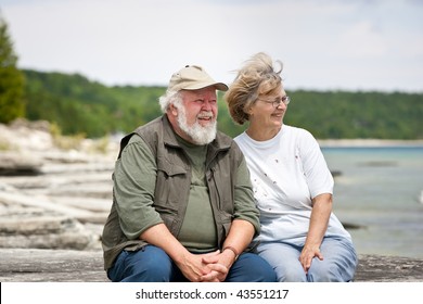 A senior couple sitting on some large shore rocks, looking out towards the water. - Powered by Shutterstock