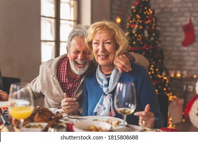 Senior couple sitting at a table by nicely decorated Christmas tree, having fun at Christmas dinner with family, laughing and enjoying their time together - Powered by Shutterstock