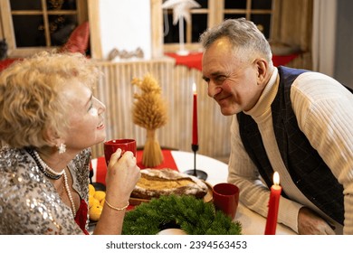 Senior couple sitting at a table by nicely decorated Christmas tree, having fun at Christmas dinner with family, laughing and enjoying their time together. - Shutterstock ID 2394563453