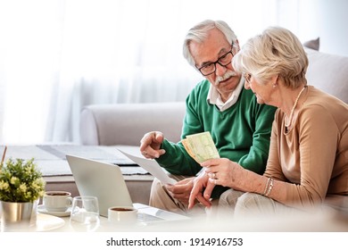 Senior couple sitting at a table at home and going through their household finances using a laptop. Senior couple going through bills while using laptop at home. - Powered by Shutterstock