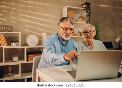 Senior couple sitting at the table at home while online shopping with a laptop and a credit card. Buying via online website and bank card, booking hotel. Focus on a man pointing to a laptop screen. - Powered by Shutterstock