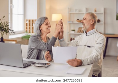 Senior couple sitting at the table with laptop and bills giving high five each other calculating finances or taxes at home. Elderly retired man and woman rejoicing income and profit on pension. - Powered by Shutterstock