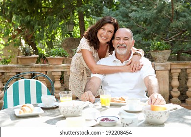 Senior couple sitting together having breakfast in a luxury hotel garden during a sunny day on holiday. Mature people eating and drinking healthy food hugging and smiling. Outdoors lifestyle. - Powered by Shutterstock