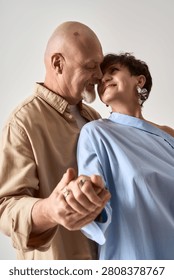 A senior couple smiles endearingly while holding hands, dressed fashionably and radiating love.