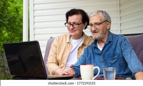 Senior Couple Smiling Looking At Laptop Computer Screen,sitting On Sofa On Home Terrace Outdoor.Сaucasian Mature And Retired Man And Woman Using Technology.Elderly Family Reading News,shopping Online