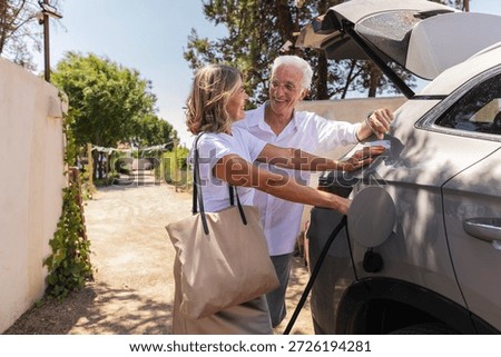 Senior couple smiling while plugging electric vehicle into charging station, embracing sustainable travel and enjoying their retirement lifestyle outdoors