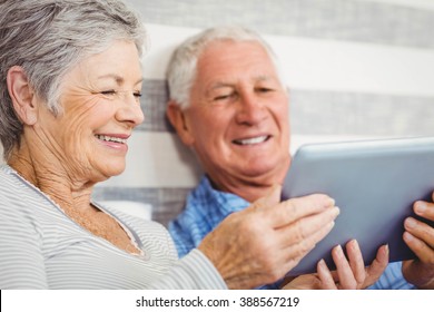 Senior couple smiling while using digital tablet in bedroom - Powered by Shutterstock