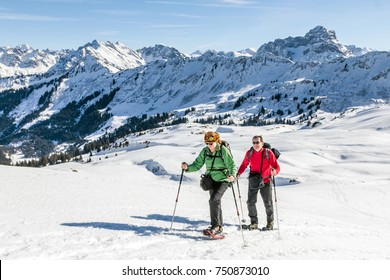 Senior Couple Is Snowshoe Hiking In Alpine Winter Mountains. Bavaria, Germany.