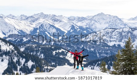 Senior couple is snowshoe hiking in alpine snow winter mountains panorama. Happy successful People with outstrechted arms. Allgau, Bavaria, Germany.