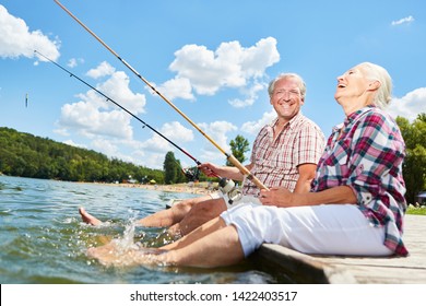 Senior Couple Splashing With Their Feet In The Water While Fishing On The Lake In Summer