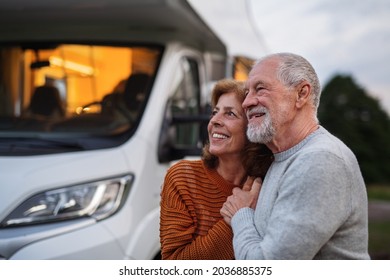 Senior Couple Standing And Hugging Outdoors At Dusk, Caravan Holiday Trip.