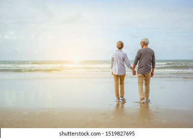 Senior couple standing on the beach holding hands at sunrise, plan life insurance at retirement concept.