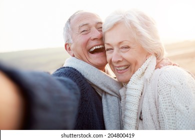 Senior Couple Standing On Beach Taking Selfie