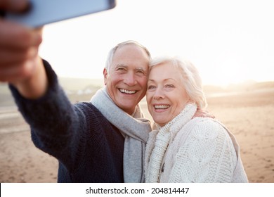 Senior Couple Standing On Beach Taking Selfie - Powered by Shutterstock