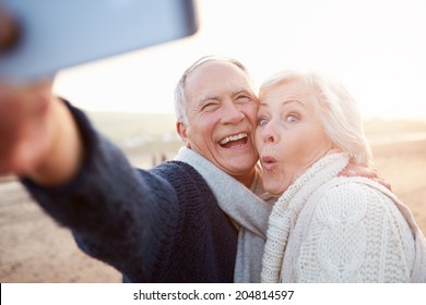 Senior Couple Standing On Beach Taking Selfie - Powered by Shutterstock