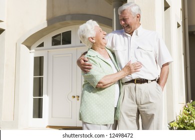 Senior Couple Standing Outside Front Door Of Home