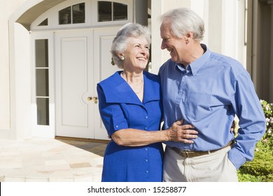 Senior Couple Standing Outside Front Door Of House