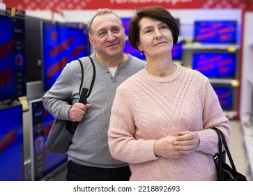 Senior Couple Standing In Salesroom Of Tech Store And Picking New TV.