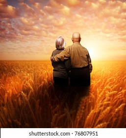 Senior Couple Standing In A Wheat Field At Sunset