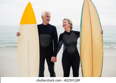Senior couple with surfboard holding hand on the beach on a sunny day