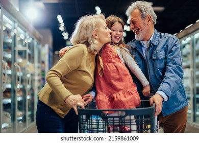 Senior couple take their granddaughter grocery shopping. Grandfather pushing cart with granddaughter and grocery in.Grandmother kissing little preschool girl