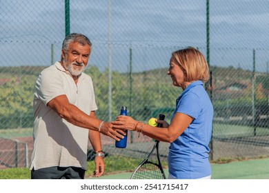 senior couple takes a break to hydrate with water bottles during their tennis match on a bright, sunny day. reflects their dedication to staying active and healthy under the warm sunlight - Powered by Shutterstock