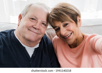 Senior couple taking a selfie with smartphone on sofa at home - Main focus on woman face