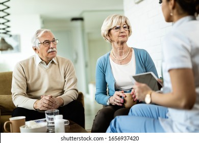 Senior Couple Talking To Healthcare Worker During Home Visit. Focus Is On Senior Woman. 