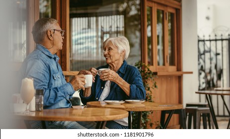 Senior Couple Talking Over A Cup Of Coffee At Cafe. Old Man And Woman Sitting At Coffee Shop Having A Conversation While Having Coffee.