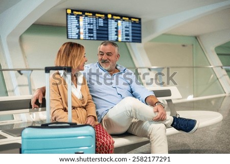 Senior couple talking and smiling while waiting for their flight at the airport terminal, they have their luggage next to them, ready to start their vacation
