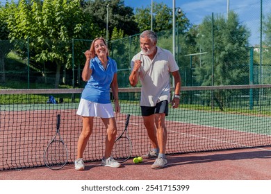 senior couple of tennis players raises their fists with big smiles in a gesture of victory after winning their match. Their joyful expressions capture the thrill of success - Powered by Shutterstock