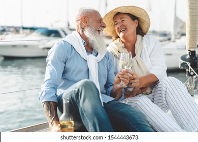 Senior couple toasting champagne on sailboat vacation - Happy elderly people having fun celebrating wedding anniversary on boat trip - Love relationship and travel lifestyle concept