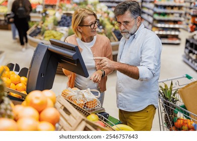 Senior couple using a digital scale to weigh oranges in the fruit and vegetable section of a grocery store, enjoying their shopping experience together - Powered by Shutterstock