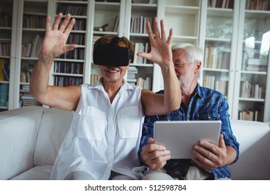 Senior couple using digital tablet and virtual reality headset in living room