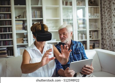 Senior Couple Using Digital Tablet And Virtual Reality Headset In Living Room